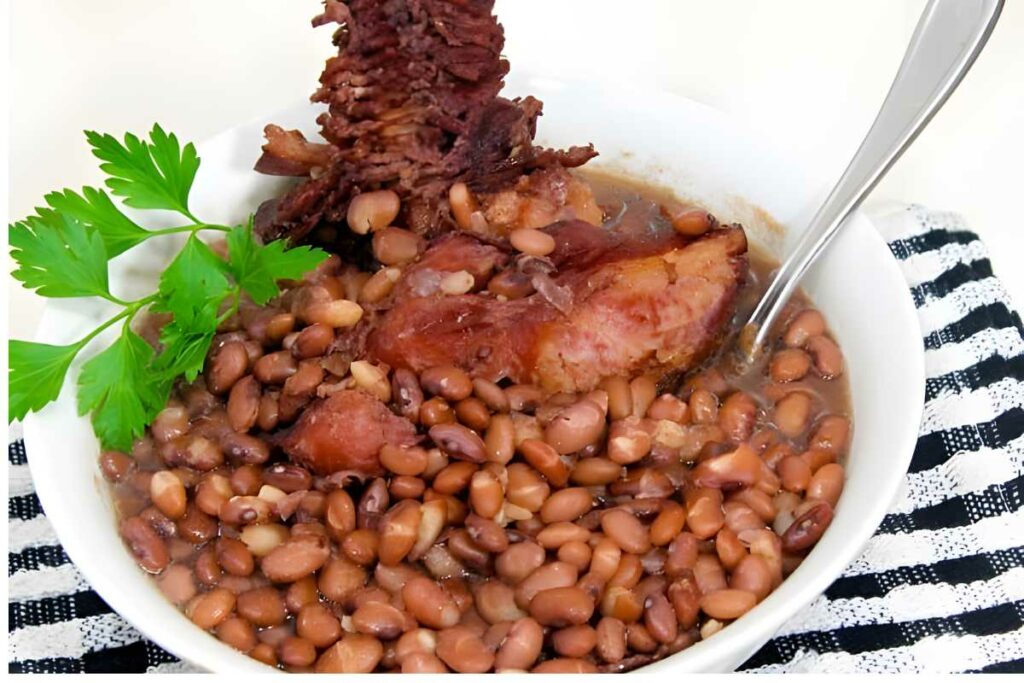 Bowl of red beans with ham hock, parsley garnish, and a spoon.