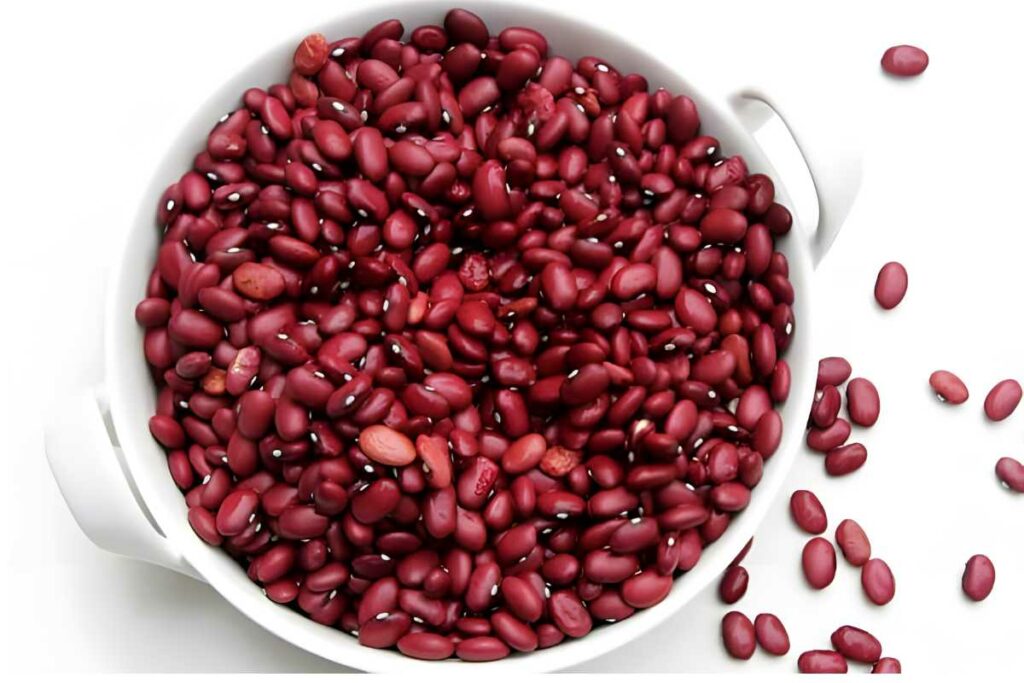 White bowl of raw red kidney beans, some scattered on white surface.