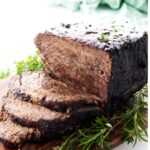Sliced German Pot roast with herbs on a wooden cutting board.