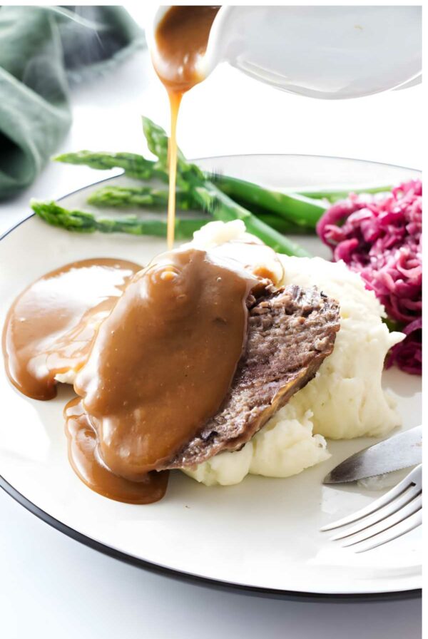German pot roast with gravy over mashed potatoes, asparagus, and cabbage on a plate.