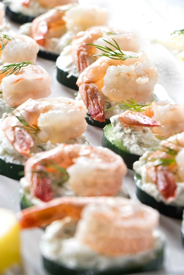 Cucumber slices with cream cheese spread, shrimp, and dill, arranged in rows.