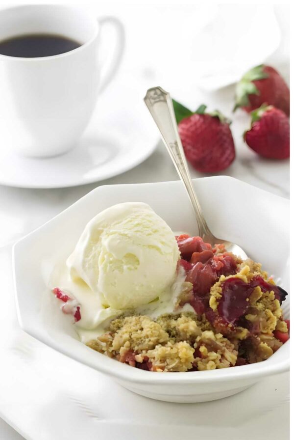 Strawberry rhubarb crisp with vanilla ice cream in a bowl, spoon inside.