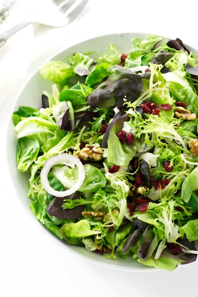 Green salad with leafy greens, red onion, walnuts, and cranberries on plate.