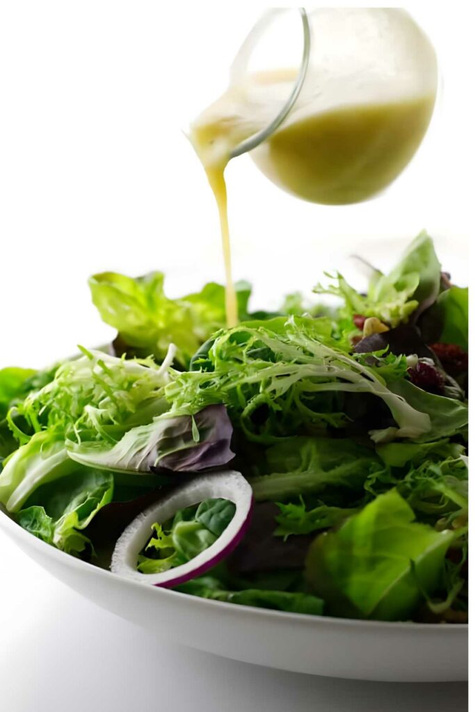 A glass pitcher pours creamy dressing over fresh tossed green salad.