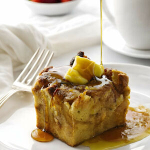 Drizzling syrup over a slice of apple french toast bake next to a cup of coffee.