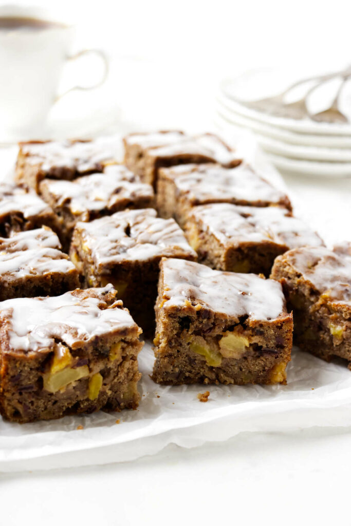 Several slices of apple date cake in front of some dessert plates.
