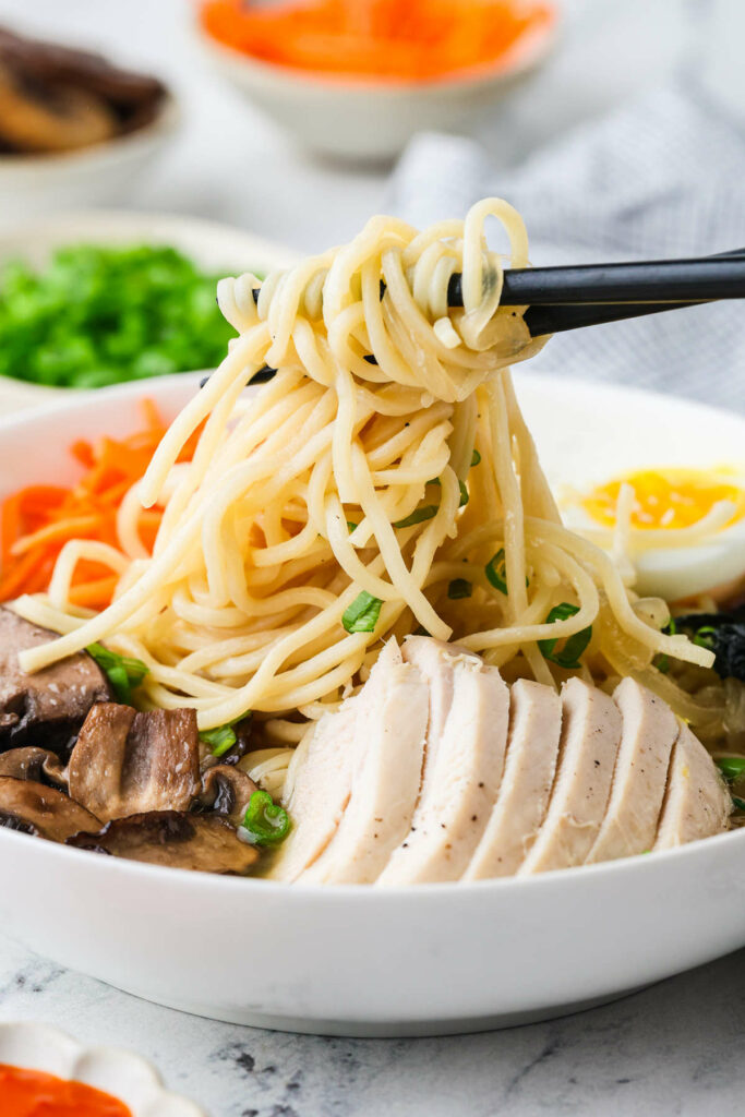 Chopsticks lifting ramen noodles from a soup bowl.