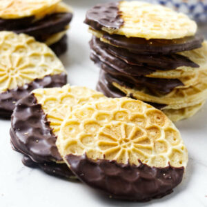 A stack of chocolate dipped pizzelle cookies on a counter.