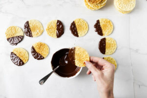 Dipping vanilla pizzelle into dark chocolate.