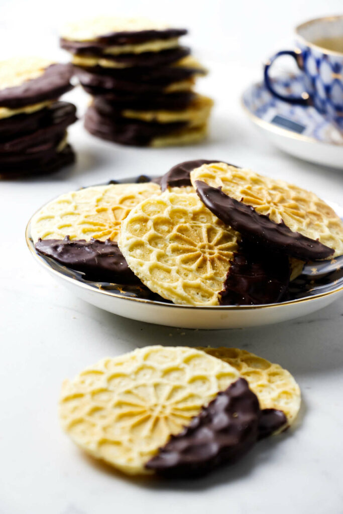 Italian waffle cookies on a plate in front of a cup of tea.