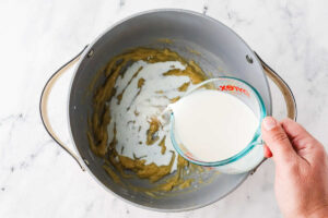 Adding milk to the roux in a pot.