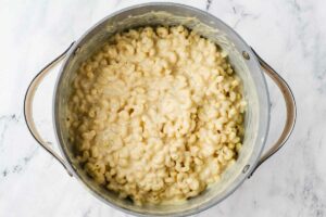 Stirring pasta into cheese sauce in a large pot.