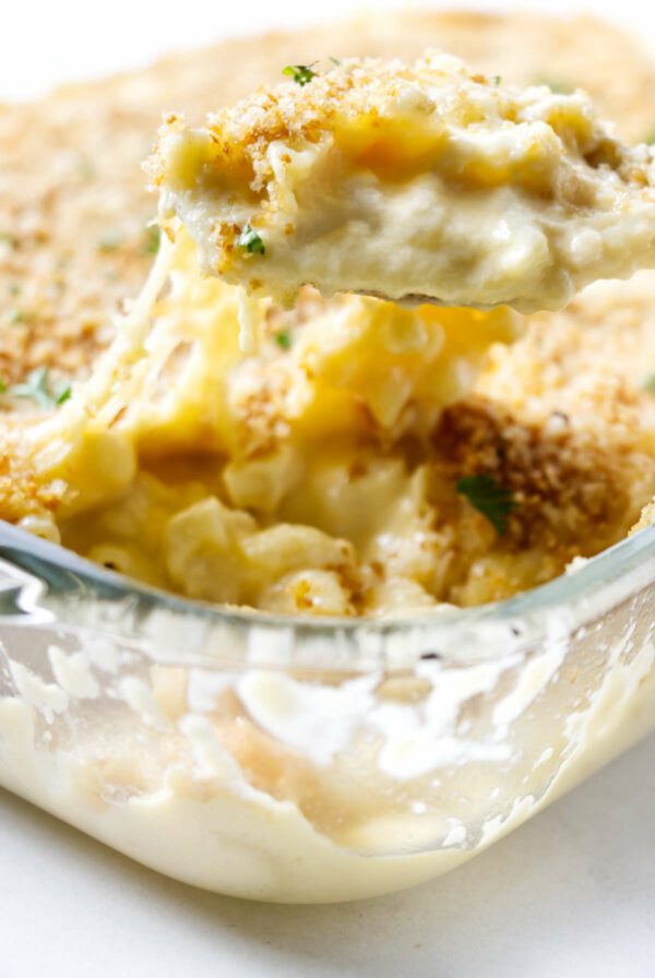 Scooping four cheese mac and cheese from a baking dish.