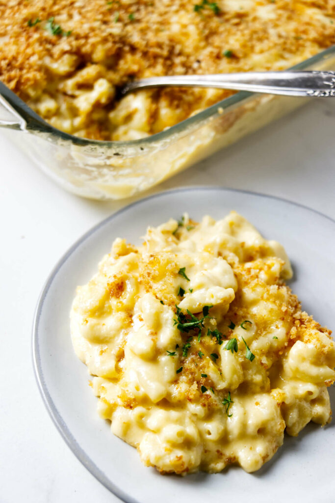 A serving of mac and cheese on a plate next to a large casserole dish.