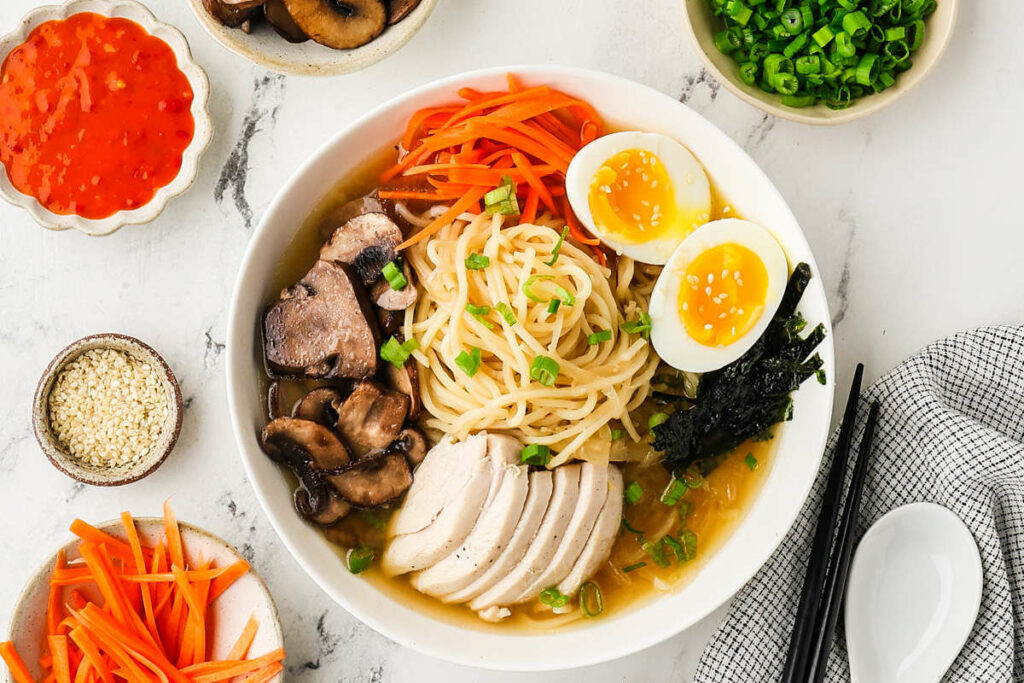 A homemade ramen dish recipe in a soup bowl with condiments.
