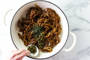 Adding fresh herbs and capers to sweet onion jam.