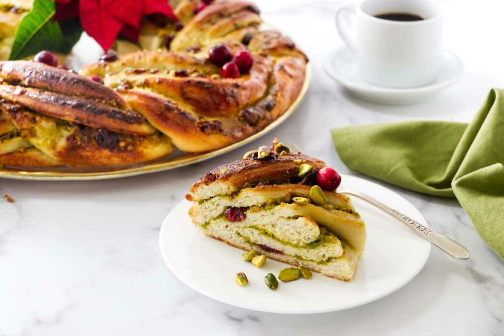 A slice of pistachio babka next to a babka wreath and coffee.