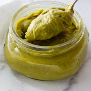 A spoon in a jar of homemade pistachio paste.