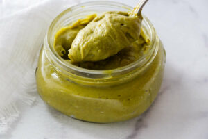 A spoon in a jar of homemade pistachio paste.
