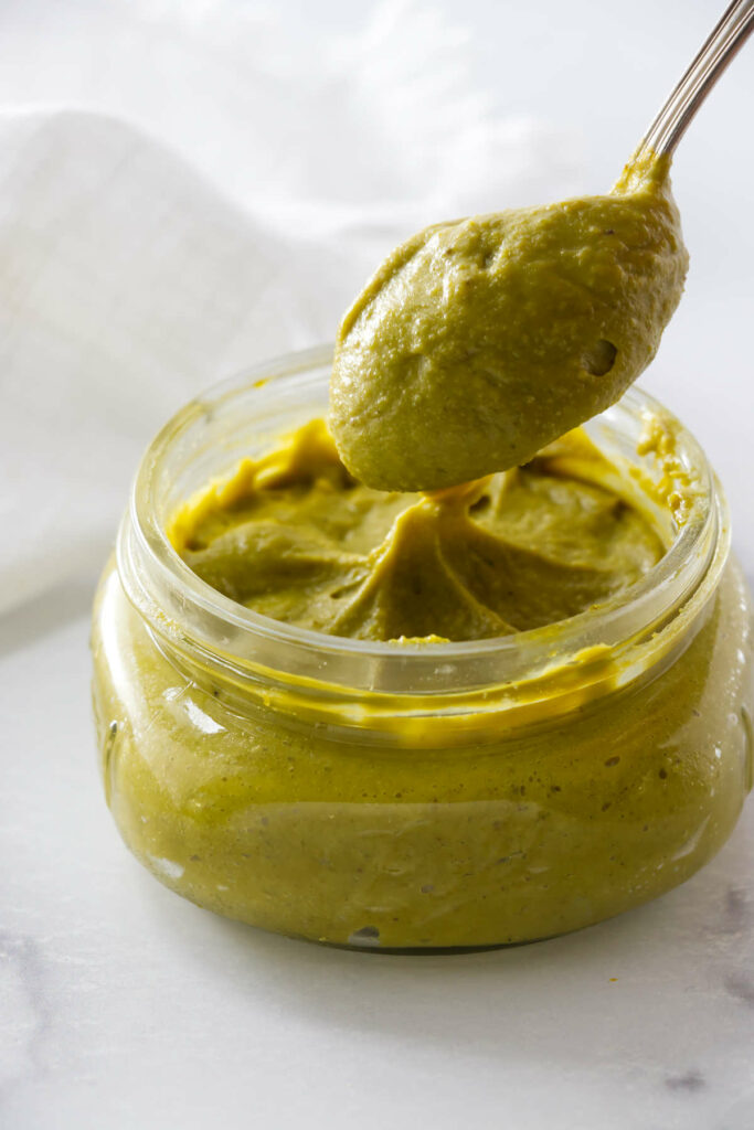A spoon over a jar of unsweetened pistachio paste.