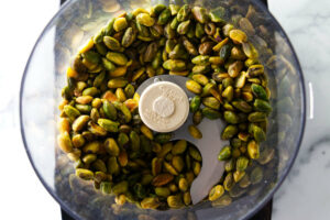 Adding the pistachios to a food processor.
