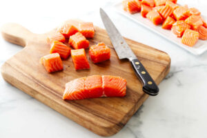Slicing a fillet of salmon into square chunks.