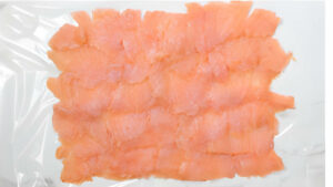 Laying cold smoked salmon into a layer on plastic wrap.