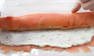 Rolling a sheet of smoked salmon up with seasoned cream cheese.