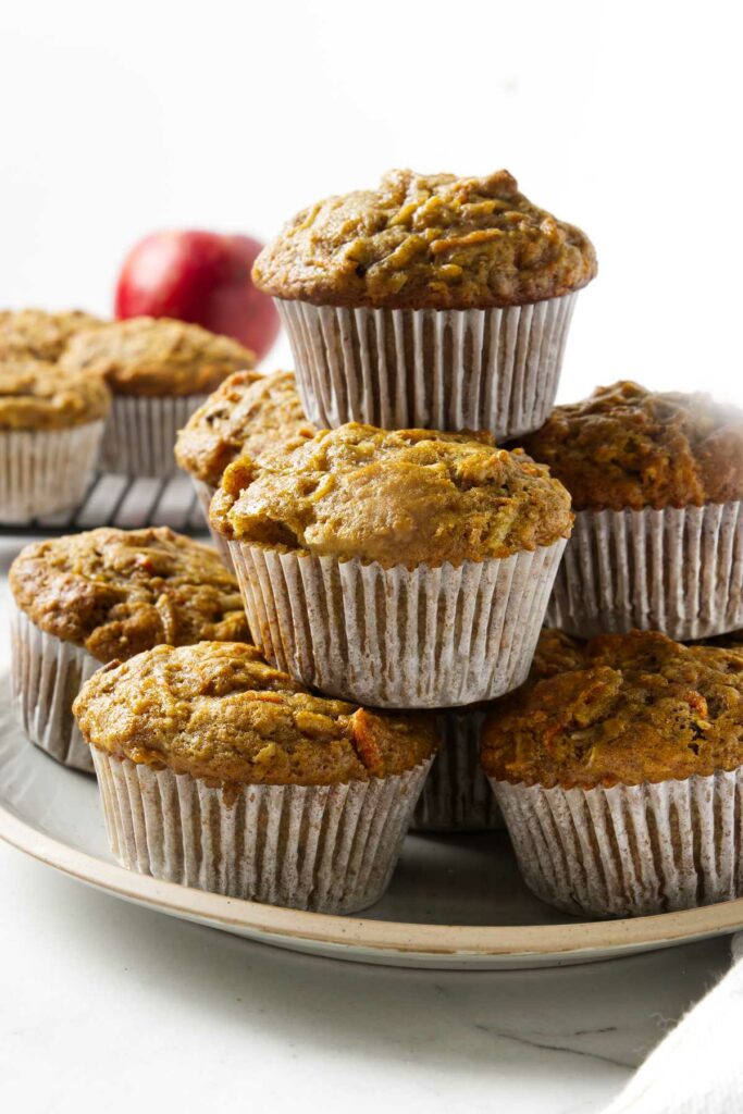 Several carrot apple muffins stacked on each other on a plate.