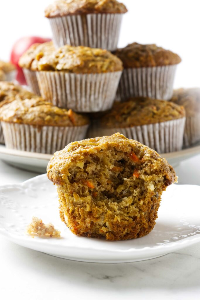 A partially eaten sourdough carrot and apple muffin with more muffins in the back.