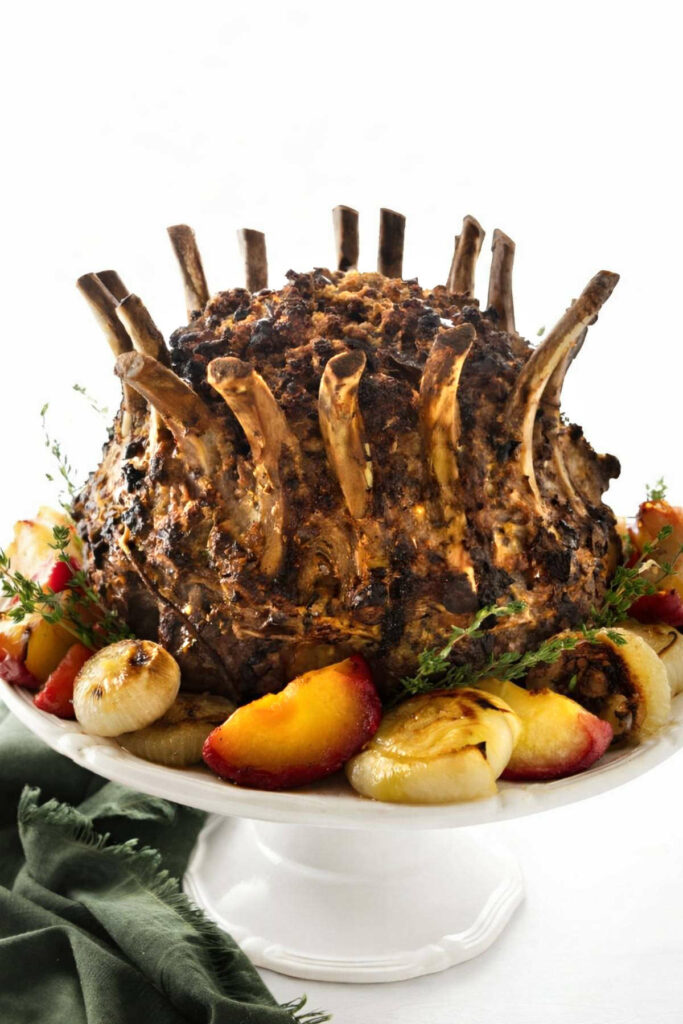 A crown pork roast on a platter with stuffing in the center and veggies on the outside.
