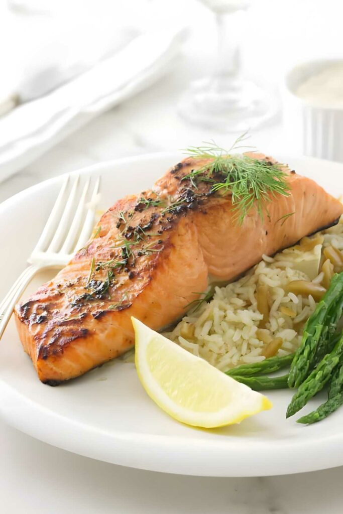 Baked salmon with herbs, rice pilaf, asparagus, lemon wedge on white plate.