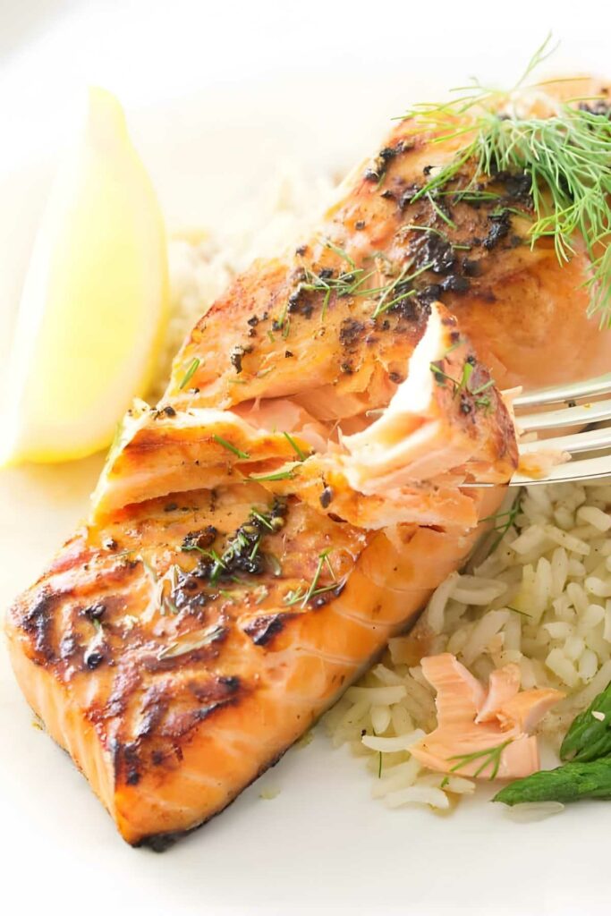 A fork flaking off a section of baked salmon.