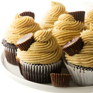 Chocolate cupcakes with light brown frosting and mini peanut butter cups on a cake stand.