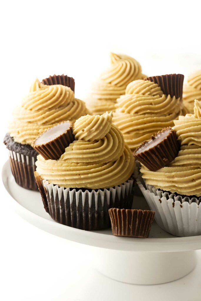 Chocolate cupcakes with peanut butter frosting and mini peanut butter cups on a cake stand.