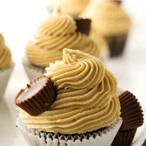 Chocolate cupcake with peanut butter frosting and mini peanut butter cups on white surface.