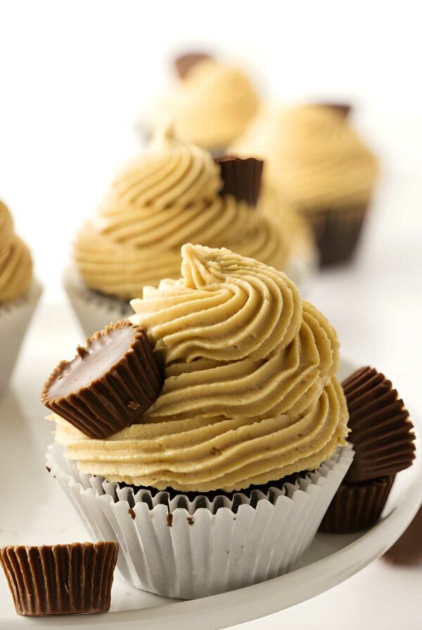 Chocolate cupcake with peanut butter frosting and mini peanut butter cups on white surface.