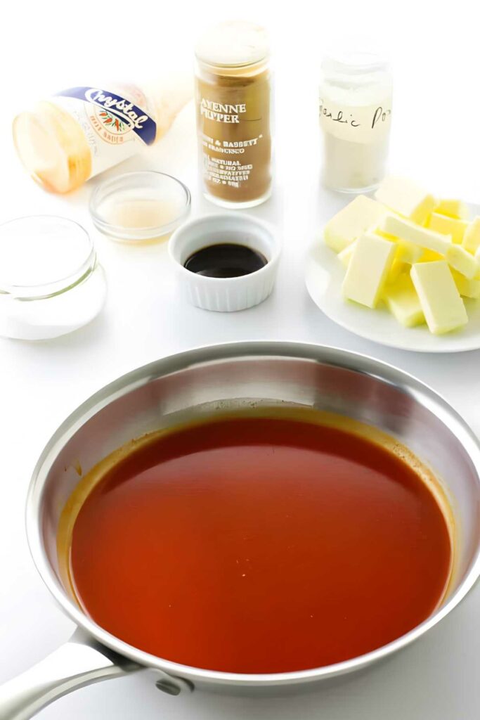 Stainless steel pan with reddish-orange sauce on white surface, spices nearby.