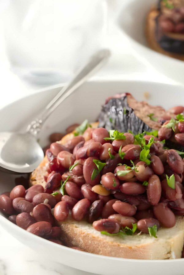 Cooked beans with parsley in a bowl on bread, spoon at edge.