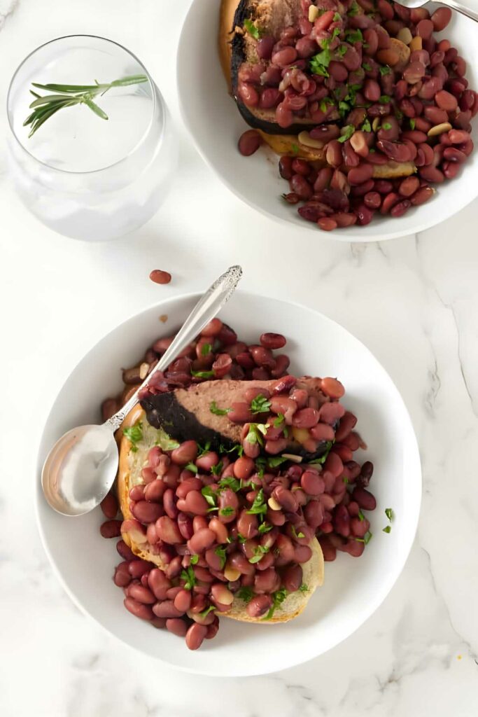 Two bowls of red beans and herbs on toast, with water and rosemary.