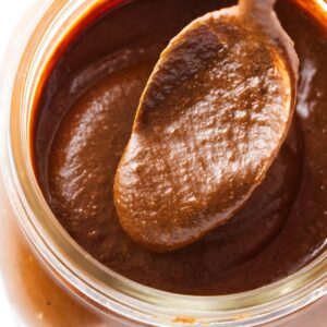 Spoon scooping creamy chocolate hazelnut spread from a glass jar.