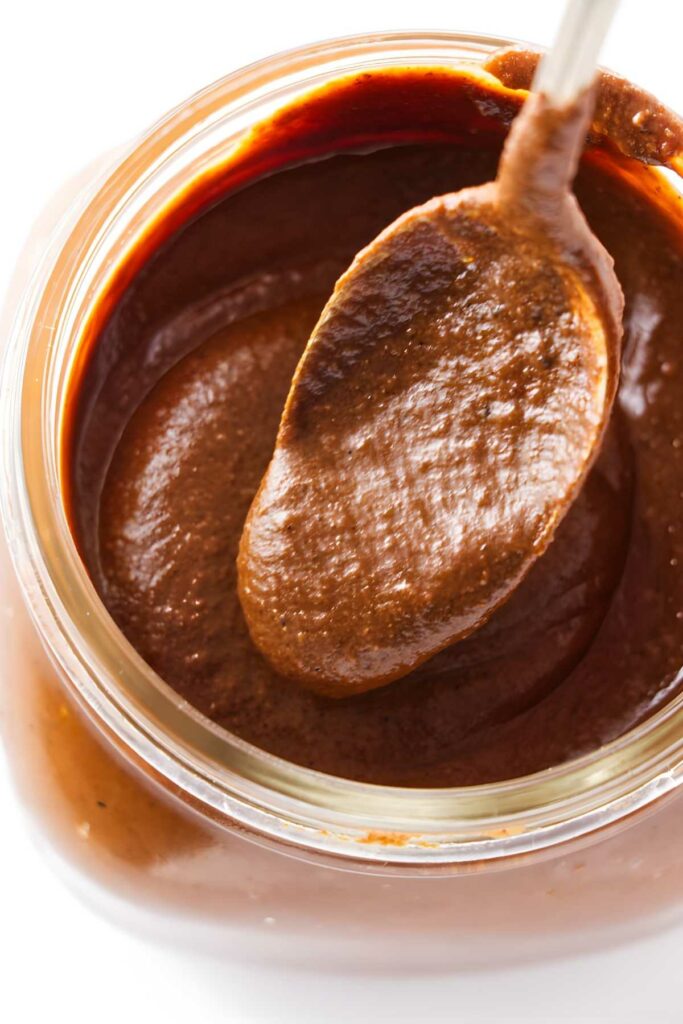 Spoon scooping mole sauce from a glass jar.