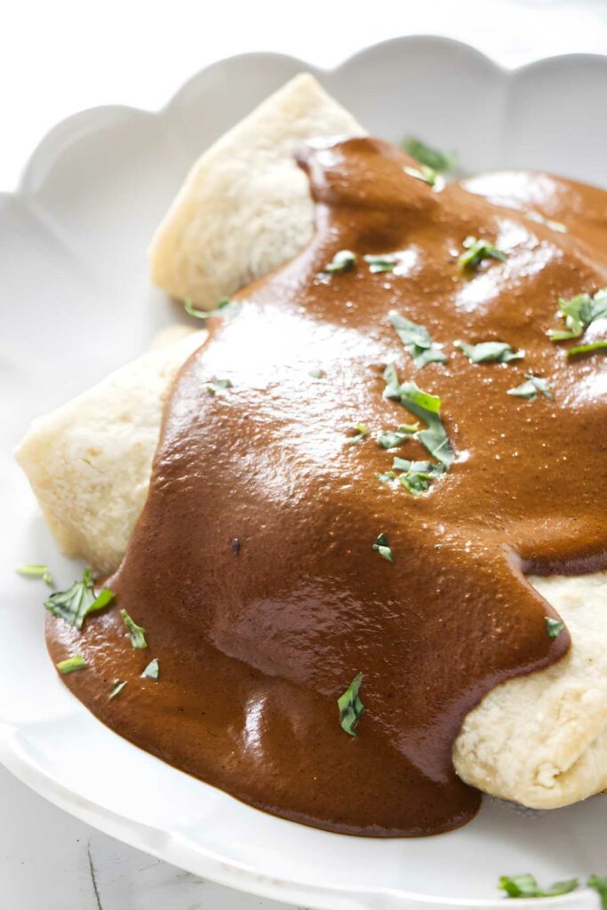 Two saucy burritos garnished with herbs on a white plate, close-up view.