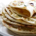 Stack of naan bread on a white plate, top piece folded to show interior.