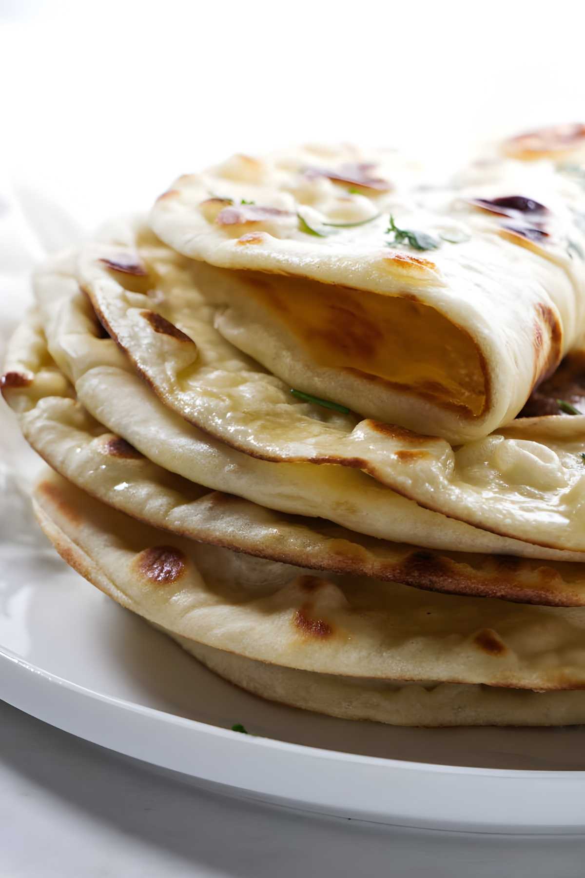Stack of naan bread on a white plate, top piece folded to show interior.