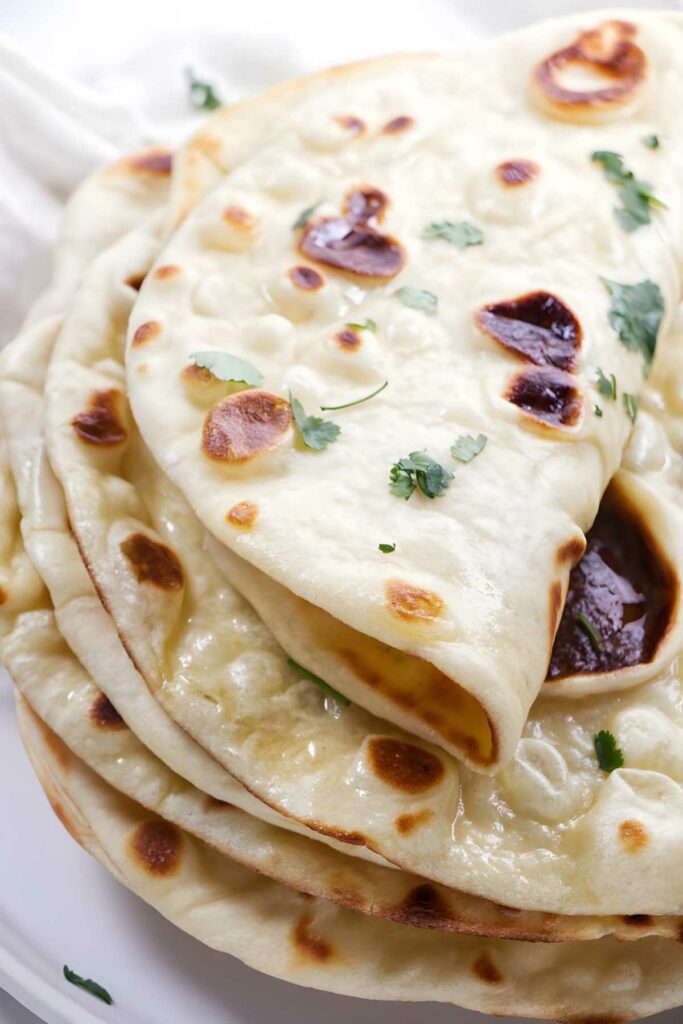 Stack of golden naan bread with cilantro on a white plate.