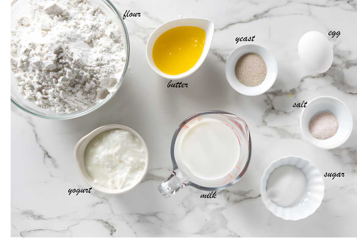 Baking ingredients labeled on a marble countertop, including flour, butter, and milk.