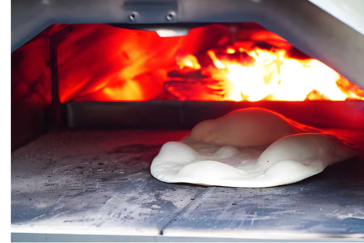 Naan baking in a wood-fired oven with glowing flames behind.