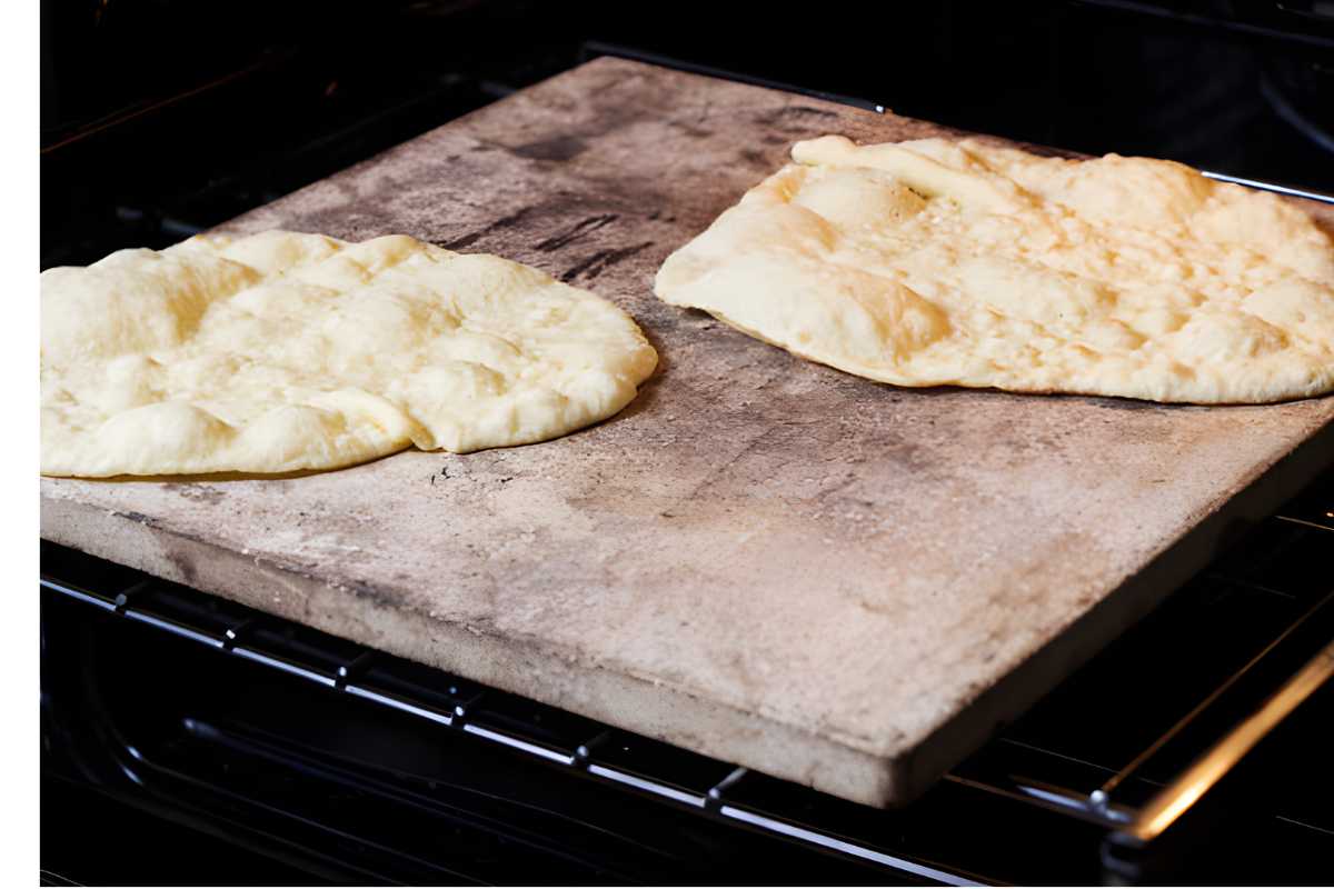 Two flatbreads baking on a pizza stone in an oven, slightly golden.