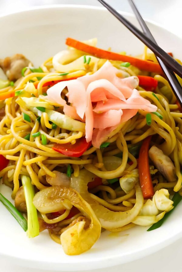 Stir-fried noodles with pork, vegetables, pickled ginger, and chopsticks.